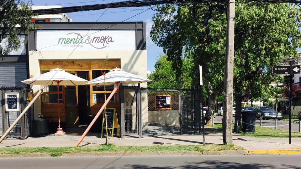 Fachada blanca de Menta & Moka con el letrero, puertas de madera y dos quitasoles blancos