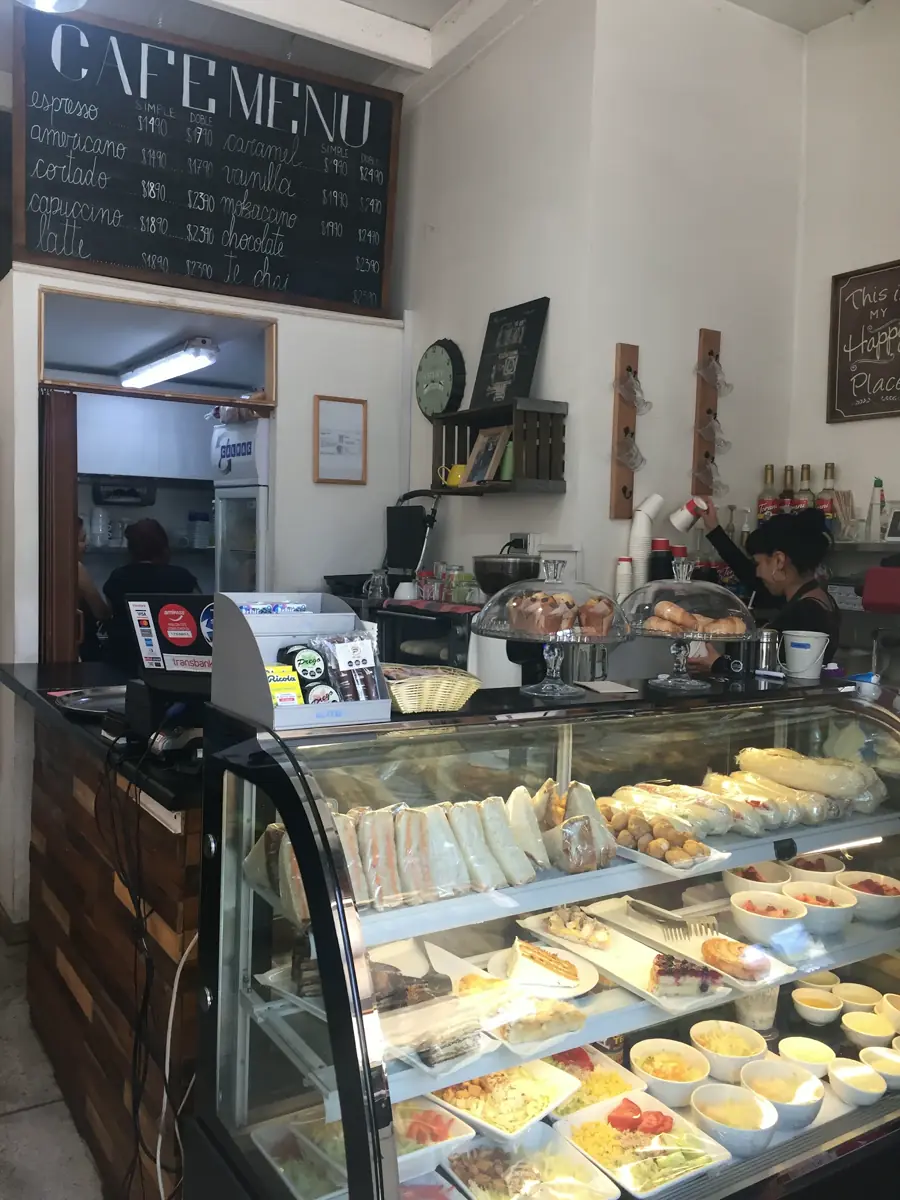 Mesón del local con la pizarra del menú de café y la vitrina de sándwiches y ensaladas