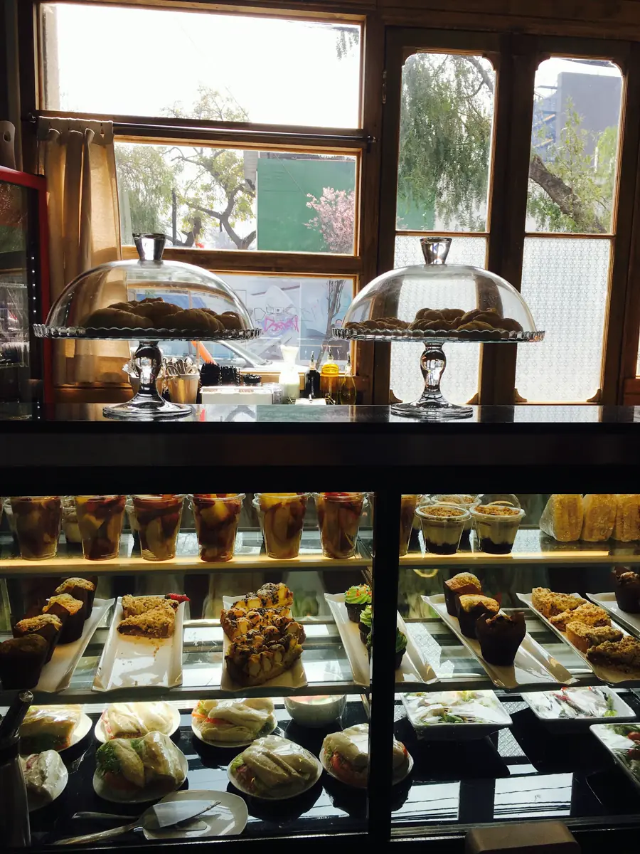 Vitrina de pastelería con queques bajo campanas de vidrio, junto a las ventanas de madera